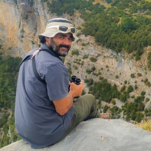 Alberto Marin, guía birding Pirineos, asomado en un acantilado con unos prismáticos